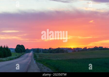 Beautiful rural asphalt road scenery at sunset or sunrise.Asphalt Road between fields trees.beautiful summer landscape with road sunset. Stock Photo