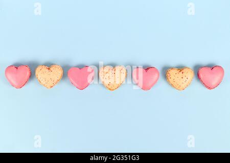 Pink and yellow heart shaped French macaron sweets in a row on blue background Stock Photo