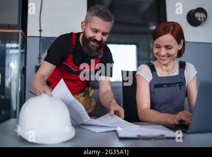 Man and woman workers or industry engineers with laptop indoors in factory, discussing issues. Stock Photo