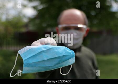 An unidentifiable man in a protective mask, glasses and gloves suggests wearing a medical mask. Coronavirus concept. Stock Photo