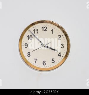 large round clock with an old, simple design and a gold frame hanging in a white wall showing accurate time Stock Photo