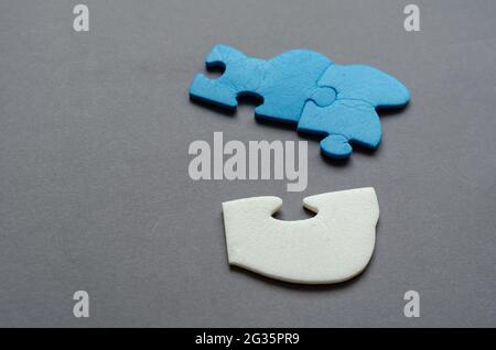 Blue and white puzzle piece on a gray background. Unconnected puzzle pieces. Side view from an angle. Selective focus. Stock Photo