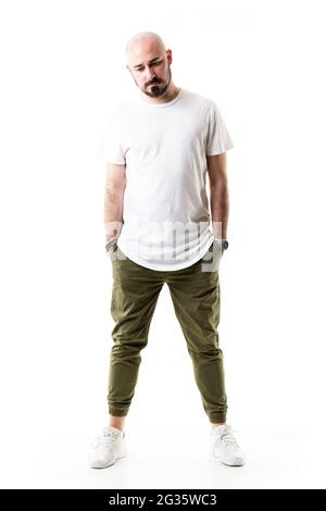 Sad shaved bald young man with hands in pockets looking down. Full body length isolated on white background Stock Photo