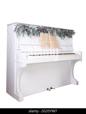 White piano isolated on white background. Spruce branches and garland. Christmas decoration. Retro piano keys are open. Musical instrument. Stock Photo