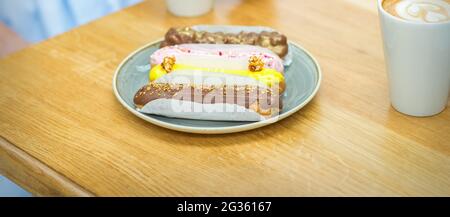 Several different eclairs on a plate are on the table with a cup of coffee in a cafe Stock Photo