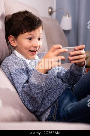 Preteen boy using smartphone on sofa at home interior Stock Photo