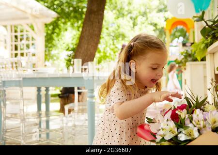 Side view of adorable little girl touching bouquet of flowers with interest in courtyard Stock Photo