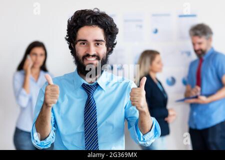 Cheering arabic businessman with beard and international team in background team at office of company Stock Photo