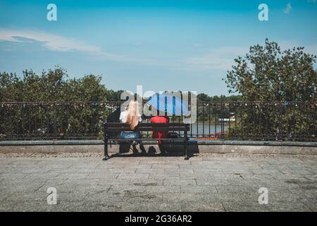 two women with umbrellas sitting on a bench on the observation deck Stock Photo
