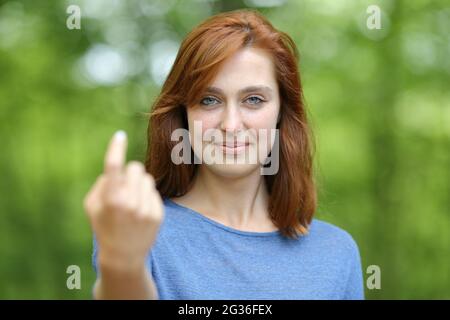 Front view portrait of a redhead woman saying come here beckoning in a forest or park Stock Photo