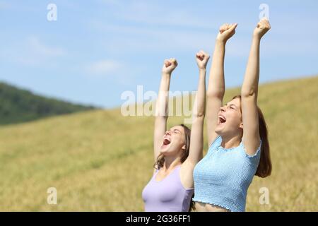 Excited friends raising arms celebrating vacation in a wheat field