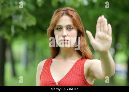 Serious redhead woman gesturing stop with her hand standing in a park Stock Photo