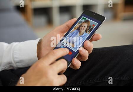 Man holding cellphone and pressing like button under young woman's picture on dating app Stock Photo