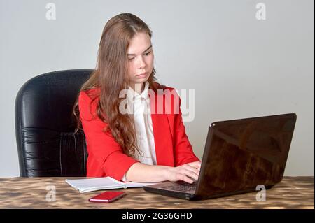 A woman sitting at a desk working with a laptop and notepad Stock Photo