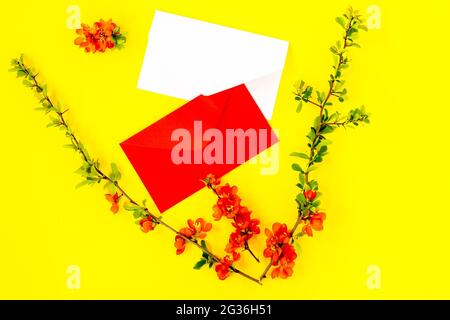 Creative flat lay of blankenvelopes frame mock up and quince tree flowers petals on yellow background with copy space in minimal style, template for l