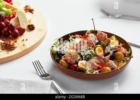 Fish salad on a light background, classic nicoise with large pieces of tuna fillet, eggs, olives and onions. Stock Photo