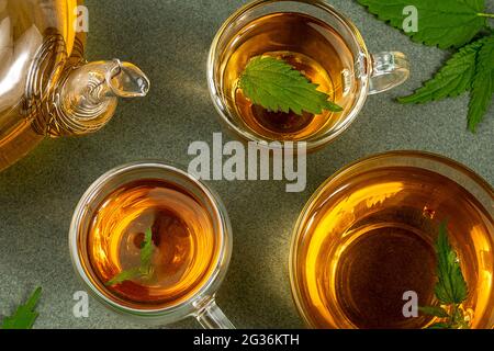 Cups of herbal tea, transparent teapot and nettle leaves on green background. Calming drink concept. Top view Flat lay. Stock Photo