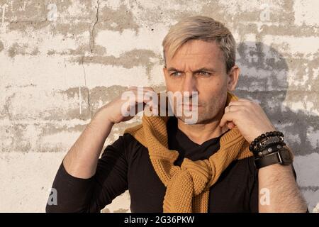 Charming stylish middle-aged blond caucasian man of model appearance in front of a white brick wall. Handsome attractive mature male model in casual f Stock Photo