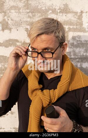 Portrait middle-aged stylish caucasian blond man takes off glasses in front of a white brick wall. Handsome attractive male model in casual fashion cl Stock Photo