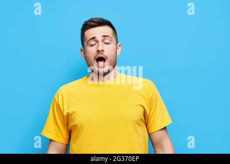 Yawning or sneezing young man over blue studio background with open mouth Stock Photo