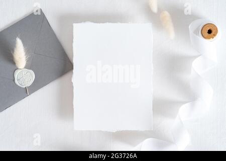 Flatlay wedding invitation card, grey envelope with seal wax stamp, dried flowers on pastel white background. Wedding stationery set top view. Stock Photo