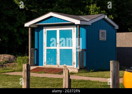Weathered blue and white shed at sunset. Ramp in front. Peeling paint on shed, wooden posts in foreground. Stock Photo