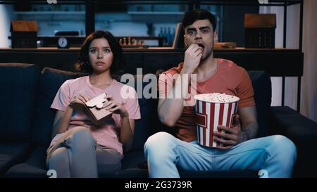 man eating popcorn near woman with chinese food in cardboard box while watching movie