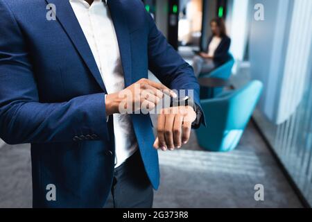 Mid section of african american businessman using smartwatch at modern office Stock Photo