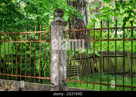There is an old forged, rusty fence between the concrete pillars. Stock Photo