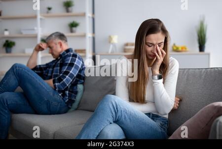 Unhappy mature woman wiping tears from her eyes on couch after conflict with her husband at home, empty space Stock Photo