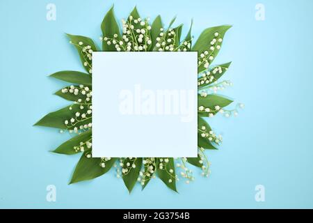 Composition with white flowers. Blank paper, lilies of the valley on a light blue background. Flat lay, top view. Stock Photo