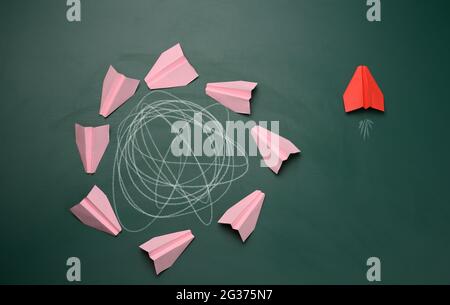 group of pink planes fly in a circle with an intricate trajectory and one flies in a straight path. The concept of thinking outside the box, uniquenes Stock Photo