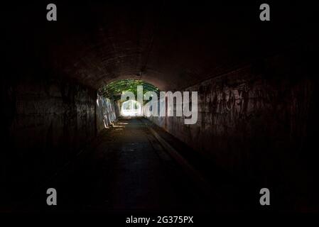 A dark tunnel with strong sunlight at the far end that allows pedestrians to cross under Victoria Road near Gladesville Hospital in Sydney, Australia Stock Photo