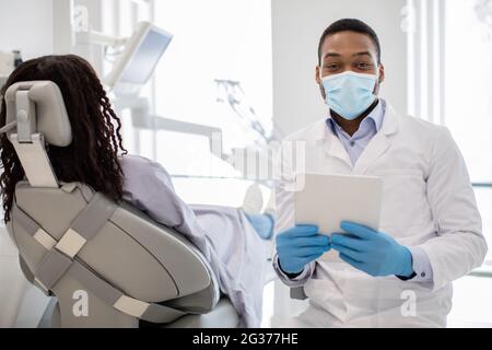 Black Dentist Doctor In Medical Mask Posing At Workplace With Digital Tablet Stock Photo