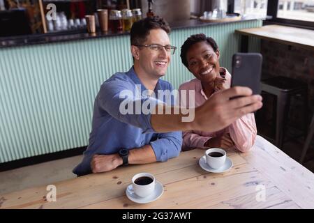 Mid section of mixed race couple smiling while taking a selfie while having coffee at a cafe Stock Photo