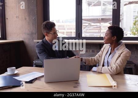 Caucasian businessman and african american businesswoman shaking hands while sitting at a cafe Stock Photo
