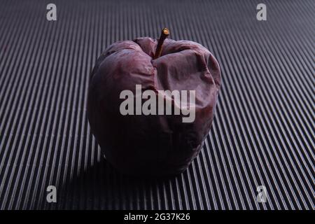 One dark rotten spoiled apple on black background.
