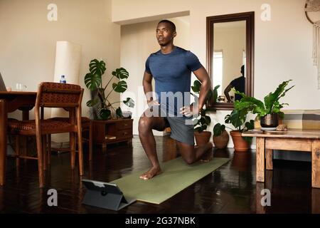 Young African man doing the crescent lunge pose at home Stock Photo