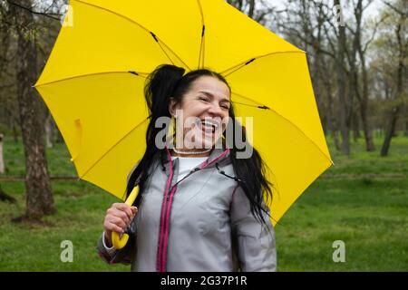 Happy senior cheerful mature, elderly, retired woman with yellow umbrella enjoying life at rainy day in park. Enjoy every moment, Enjoying life Stock Photo