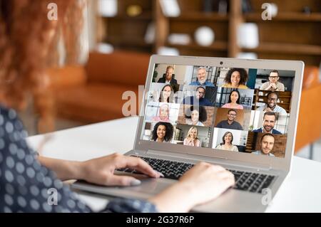 Red-haired curly woman sitting at the laptop, chatting with friends or colleagues via video meeting, discussing the new project, teaching online,making video call to group of diverse people Stock Photo