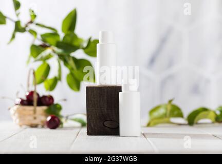 White tubes with cosmetics on a wooden podium against the background of foliage, cherry berries. Natural cosmetics.  Stock Photo