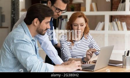 Concentrated three millennial employees preparing presentation on computer. Stock Photo