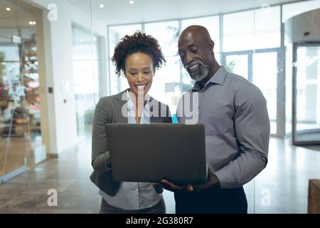 Two diverse male and female business colleagues using laptop and smiling Stock Photo