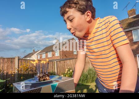 A boy blows out candles on a slice of birthday cake outside in the garden, Stock Photo