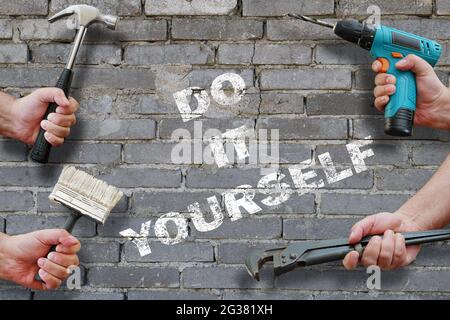 hands holding tools on grey brickwall background with writing do it yourself on it Stock Photo