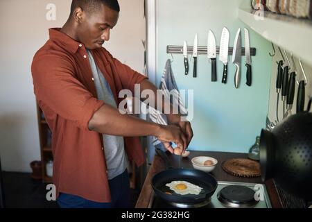 Young African man cracking eggs into a frypan for breakfast Stock Photo