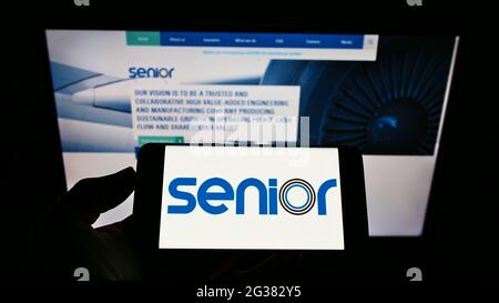 Person holding cellphone with logo of British manufacturing company Senior plc on screen in front of business webpage. Focus on phone display. Stock Photo