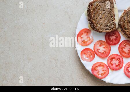 top view of slices of bread made from spelled flour filled with cheese, next to sliced tomatoes, on a white porcelain plate. Stock Photo