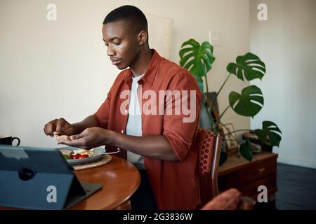 Young African man eating breakfast and using a digital tablet Stock Photo