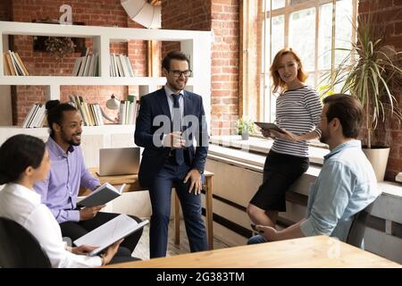 Smiling relaxed millennial diverse teammates involved in friendly conversation. Stock Photo